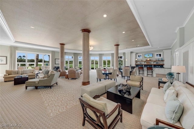 carpeted living room with ornate columns, a raised ceiling, a healthy amount of sunlight, and crown molding