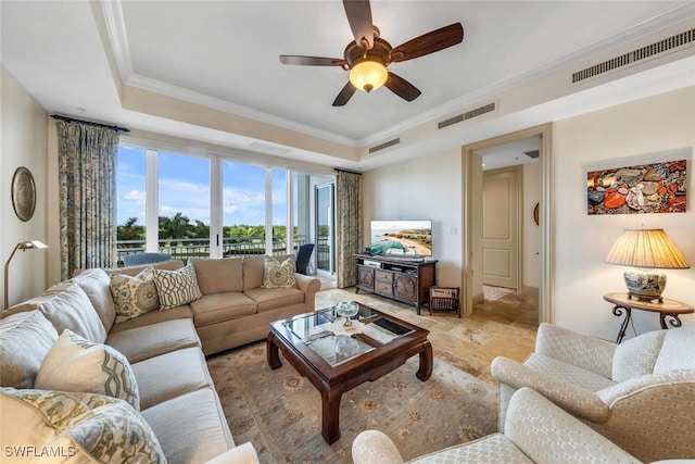 tiled living room with ceiling fan, a raised ceiling, and ornamental molding