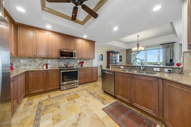 kitchen with sink, appliances with stainless steel finishes, hanging light fixtures, light stone counters, and a tray ceiling