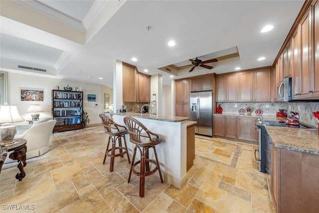 kitchen with a breakfast bar area, stainless steel appliances, light stone counters, kitchen peninsula, and a raised ceiling