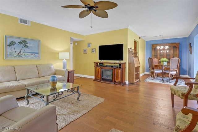 living room with wood-type flooring, ornamental molding, and ceiling fan with notable chandelier