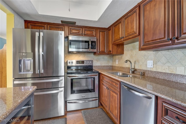 kitchen featuring appliances with stainless steel finishes, hardwood / wood-style floors, sink, backsplash, and light stone counters