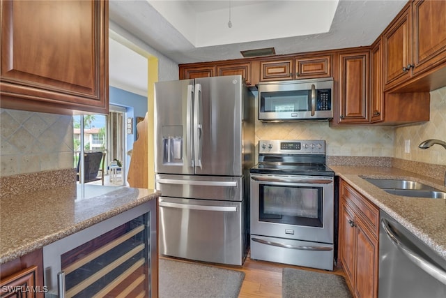 kitchen featuring sink, backsplash, beverage cooler, light stone counters, and stainless steel appliances