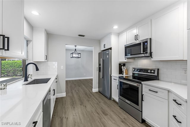 kitchen with hanging light fixtures, sink, appliances with stainless steel finishes, light hardwood / wood-style floors, and white cabinetry