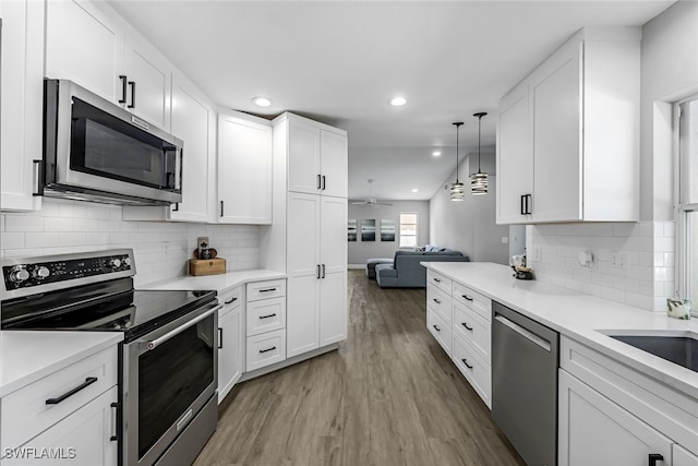 kitchen with white cabinetry, hanging light fixtures, stainless steel appliances, and wood-type flooring