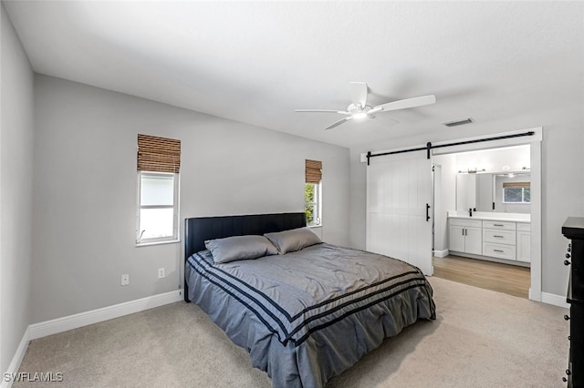 carpeted bedroom featuring a barn door, ceiling fan, and ensuite bathroom