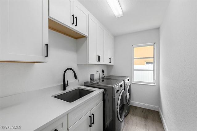 clothes washing area featuring hardwood / wood-style flooring, cabinets, independent washer and dryer, and sink