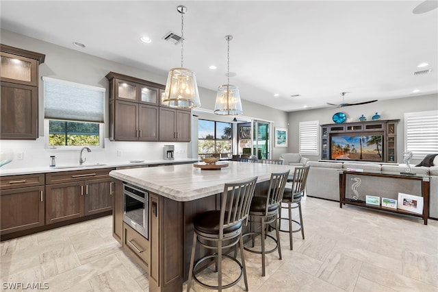 kitchen featuring sink, hanging light fixtures, stainless steel microwave, light tile patterned floors, and a center island