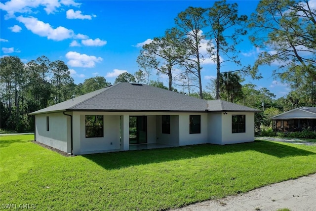 rear view of property with a lawn, a shingled roof, and stucco siding