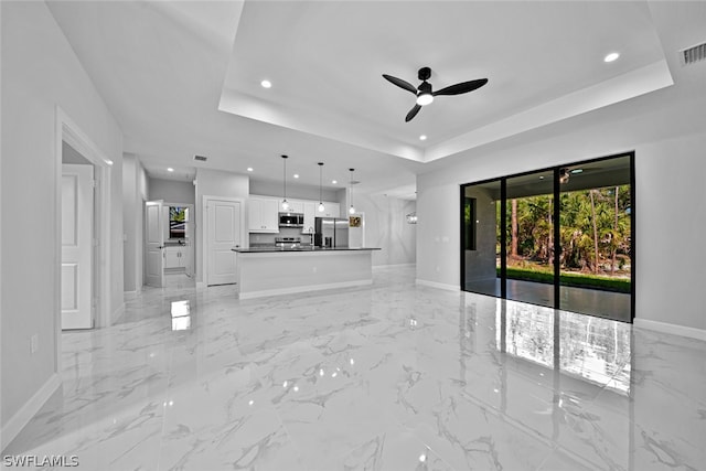 unfurnished living room with light tile patterned flooring, ceiling fan, and a raised ceiling