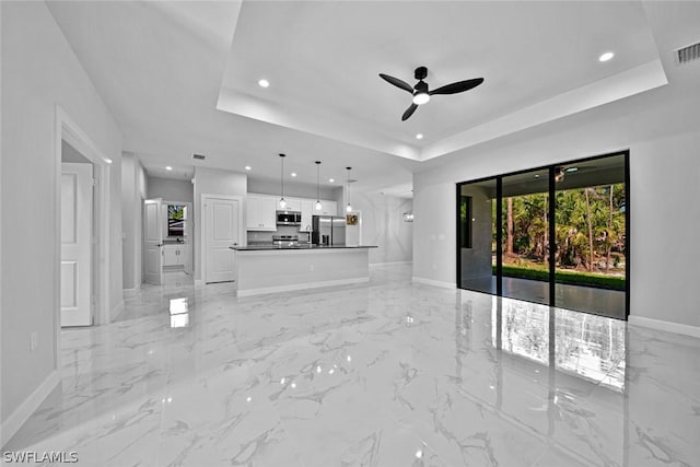 unfurnished living room featuring recessed lighting, baseboards, a raised ceiling, and ceiling fan