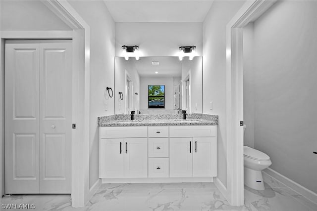 bathroom with double vanity, toilet, marble finish floor, and a sink