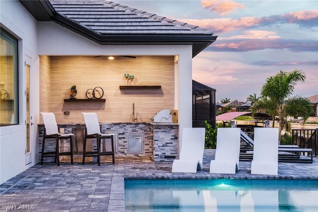 pool at dusk with a bar, area for grilling, and a patio area