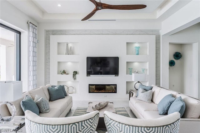 living room with a tray ceiling, built in features, and ceiling fan