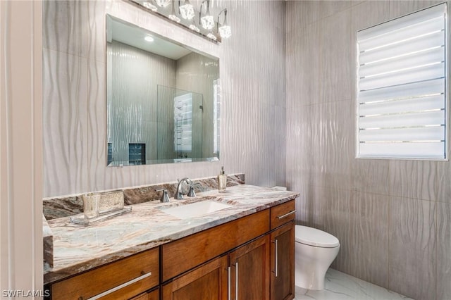 bathroom with vanity, a shower, tile walls, and toilet