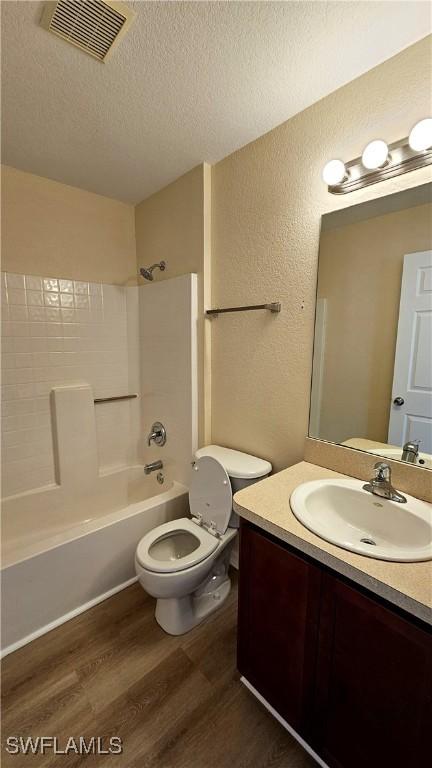 full bathroom featuring washtub / shower combination, wood-type flooring, a textured ceiling, toilet, and vanity