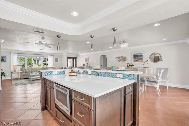 kitchen featuring crown molding, light tile patterned floors, stainless steel microwave, a kitchen island, and ceiling fan