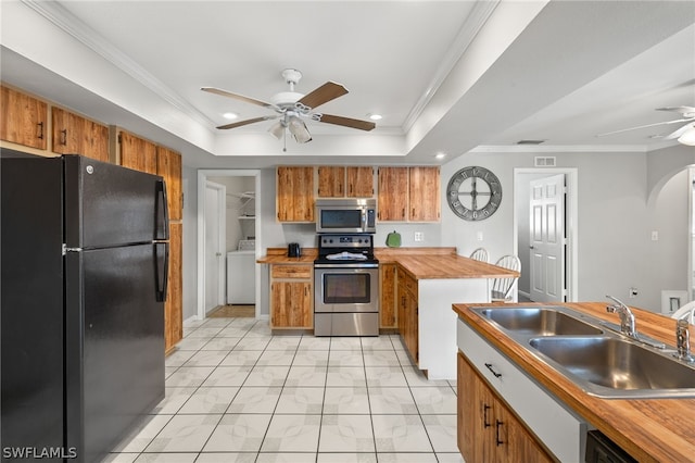 kitchen featuring ceiling fan, stainless steel appliances, a sink, a tray ceiling, and washer / dryer