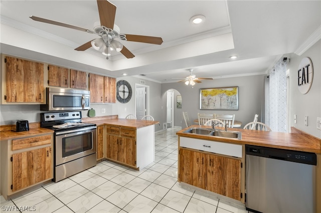 kitchen featuring stainless steel appliances, a tray ceiling, a sink, and a peninsula