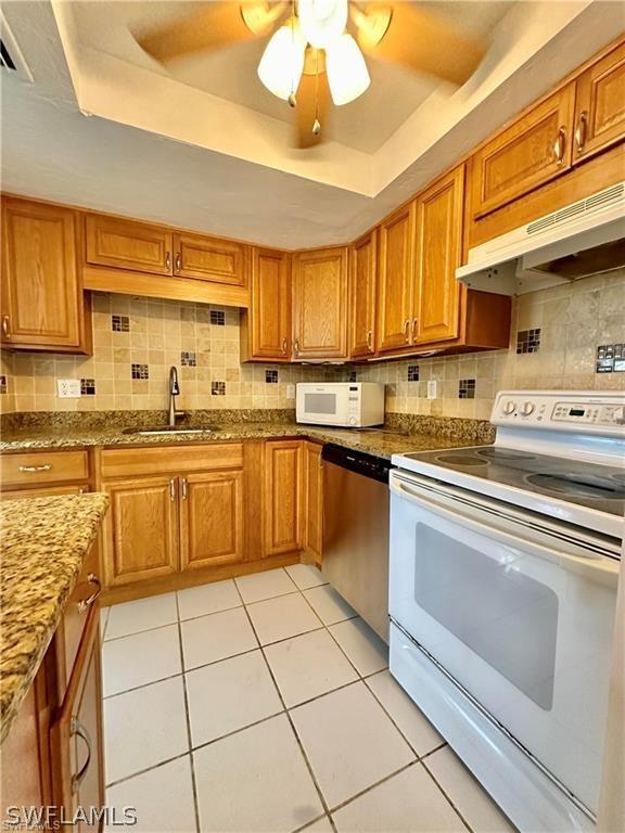 kitchen featuring ceiling fan, sink, white appliances, a tray ceiling, and light tile patterned flooring