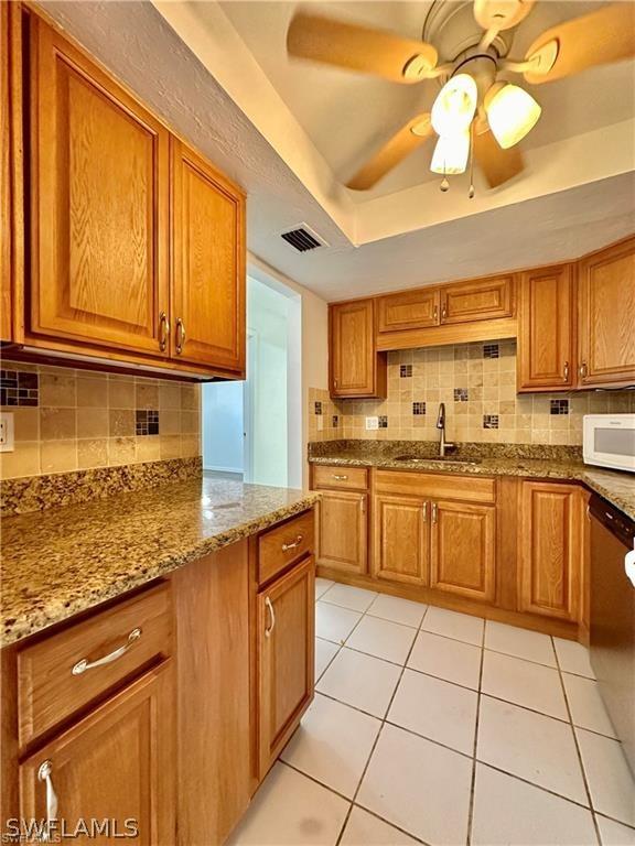 kitchen with decorative backsplash, light stone counters, ceiling fan, sink, and light tile patterned floors