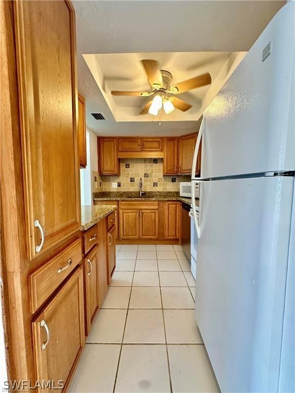 kitchen with white appliances, backsplash, stone counters, sink, and light tile patterned floors