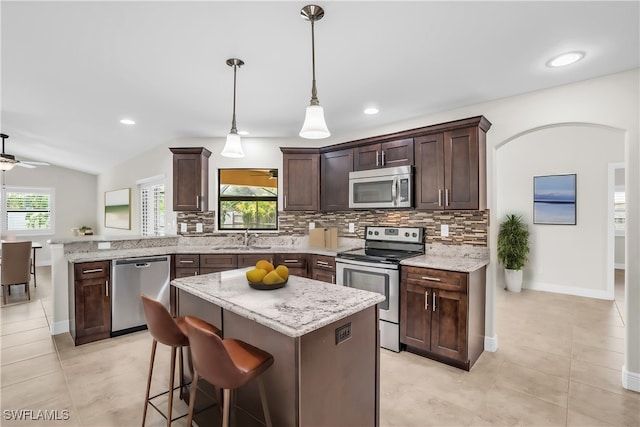 kitchen featuring sink, pendant lighting, vaulted ceiling, a kitchen island, and appliances with stainless steel finishes