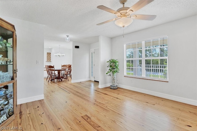 interior space with a textured ceiling, ceiling fan with notable chandelier, and light hardwood / wood-style floors