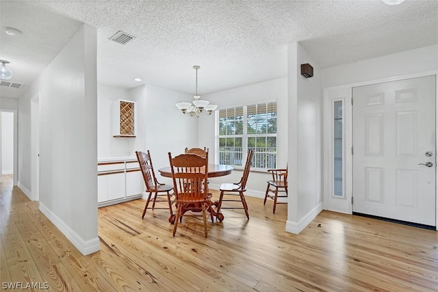 dining area featuring a notable chandelier, a textured ceiling, and light wood-type flooring