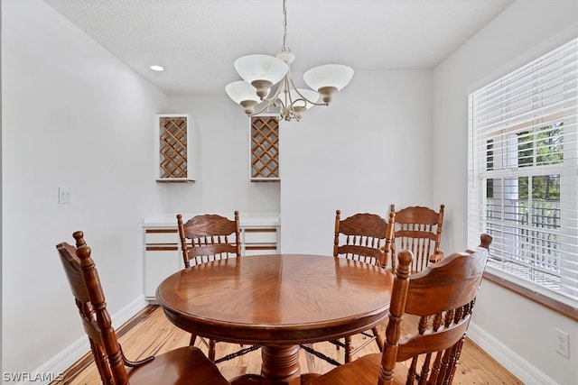 dining space with an inviting chandelier, a textured ceiling, and light hardwood / wood-style flooring