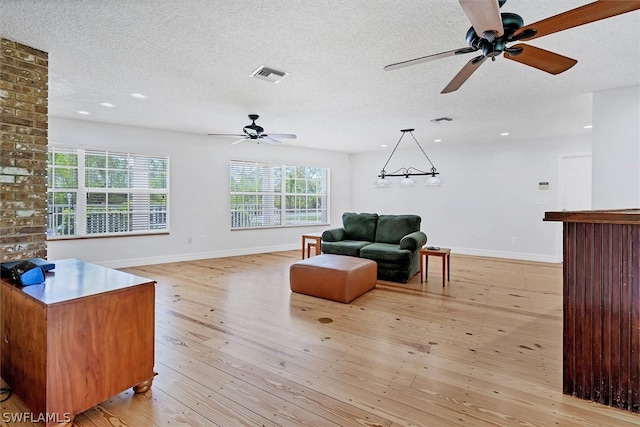 living room featuring a textured ceiling, a healthy amount of sunlight, ceiling fan, and light wood-type flooring