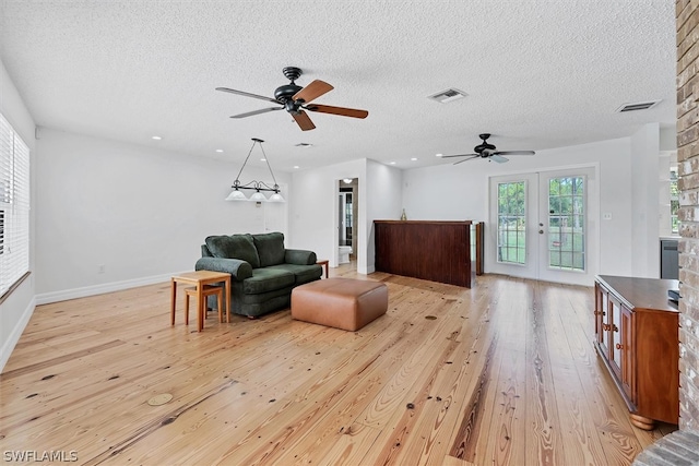 living area featuring light hardwood / wood-style flooring, a textured ceiling, ceiling fan, and french doors