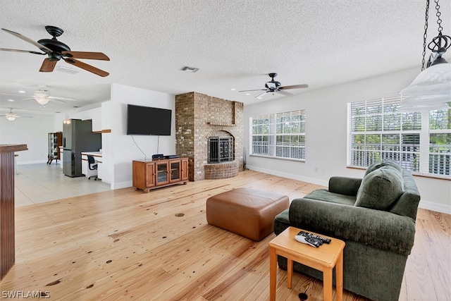 living room featuring a textured ceiling, light hardwood / wood-style flooring, a brick fireplace, and ceiling fan