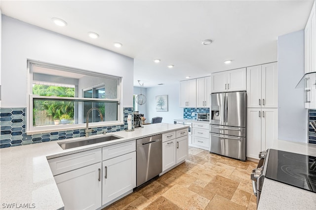 kitchen with appliances with stainless steel finishes, sink, white cabinets, backsplash, and light stone countertops