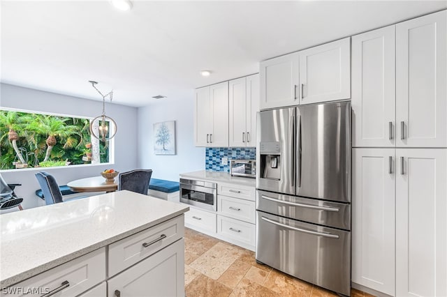 kitchen featuring light stone counters, hanging light fixtures, stainless steel fridge, decorative backsplash, and white cabinets