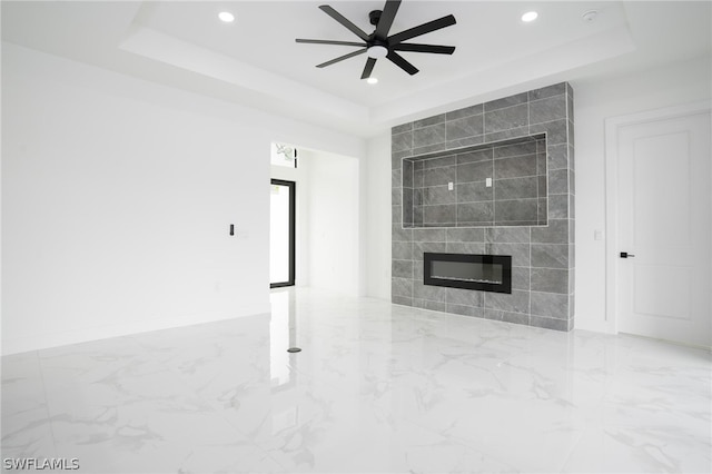 unfurnished living room with ceiling fan, a tray ceiling, and a tile fireplace