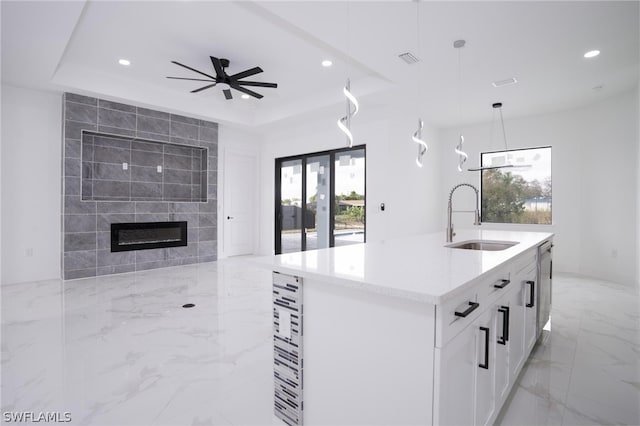 kitchen featuring white cabinets, a kitchen island with sink, a tray ceiling, decorative light fixtures, and sink