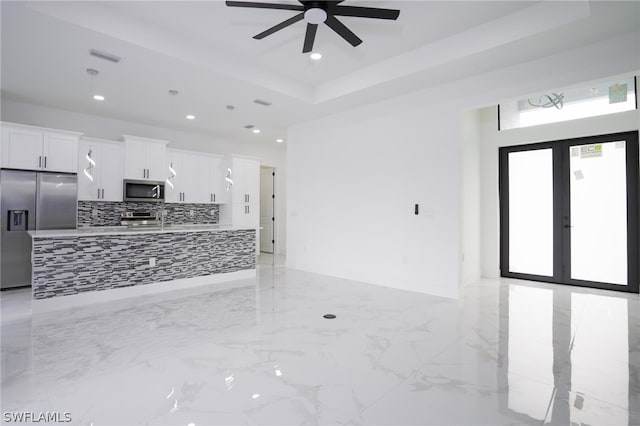 kitchen featuring appliances with stainless steel finishes, backsplash, a tray ceiling, ceiling fan, and white cabinets