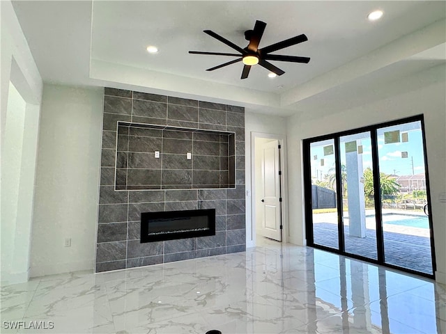 unfurnished living room featuring tile walls, a fireplace, a tray ceiling, and ceiling fan