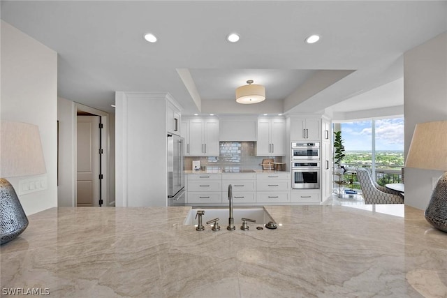 kitchen featuring appliances with stainless steel finishes, white cabinetry, sink, backsplash, and light stone counters