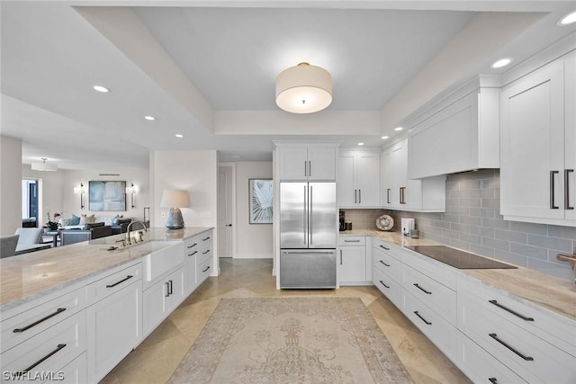 kitchen featuring tasteful backsplash, white cabinetry, built in refrigerator, light stone countertops, and black electric cooktop