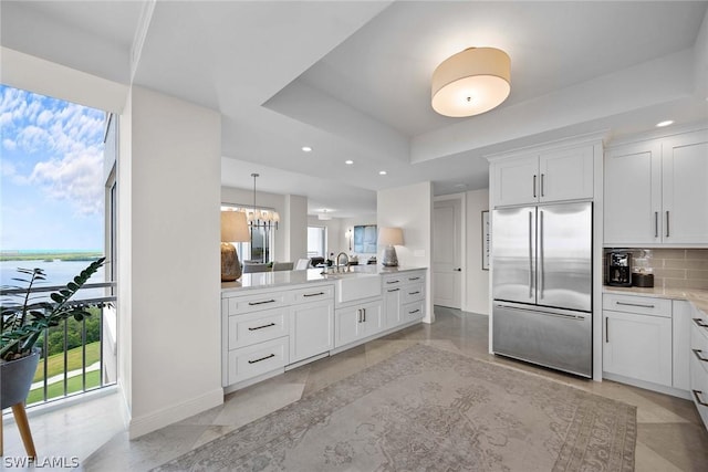 kitchen featuring tasteful backsplash, white cabinetry, stainless steel built in refrigerator, a tray ceiling, and a water view