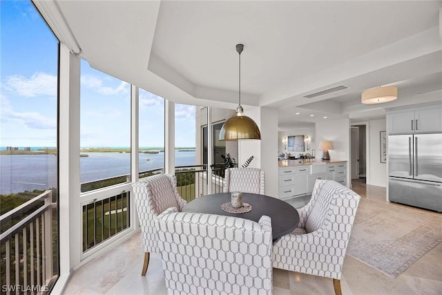 dining space featuring sink, a wall of windows, a raised ceiling, and a water view