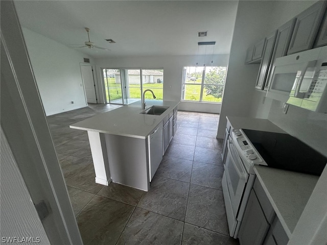 kitchen with ceiling fan, sink, dark tile patterned floors, an island with sink, and white appliances