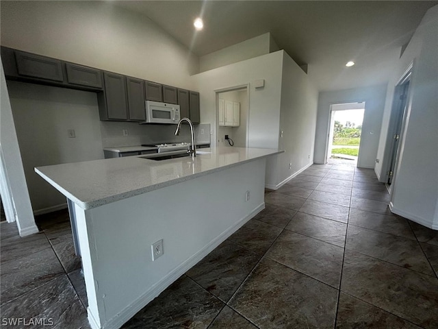 kitchen with gray cabinets, sink, an island with sink, and vaulted ceiling