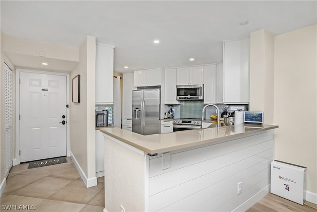 kitchen with appliances with stainless steel finishes, tasteful backsplash, sink, white cabinets, and kitchen peninsula