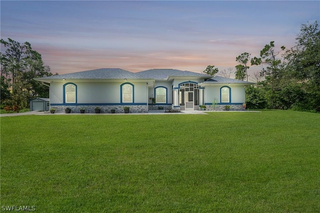 view of front of house with a yard, stone siding, an outdoor structure, and stucco siding