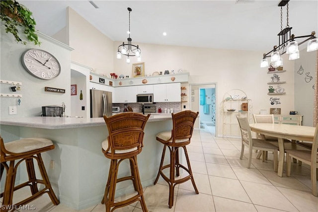 kitchen featuring appliances with stainless steel finishes, decorative light fixtures, light tile patterned floors, a kitchen breakfast bar, and white cabinetry