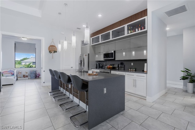 kitchen featuring a kitchen bar, appliances with stainless steel finishes, a center island with sink, sink, and backsplash