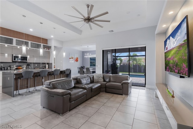 tiled living room featuring ceiling fan with notable chandelier and sink